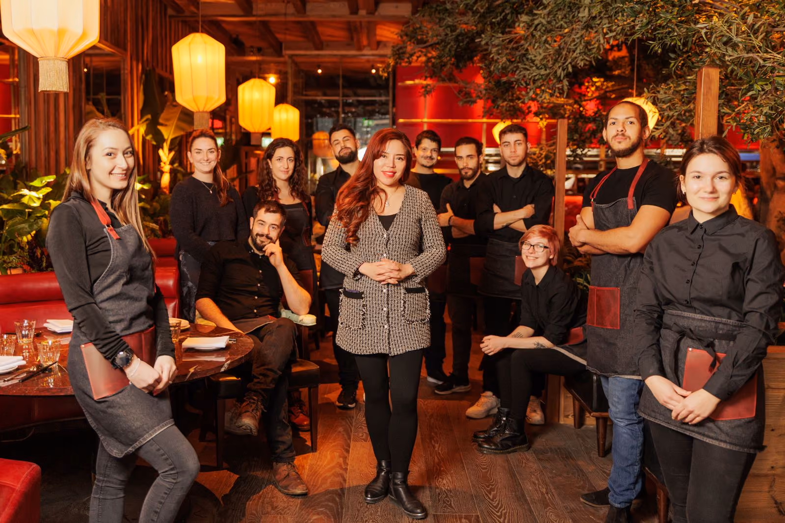 Front-of-house team in black aprons gathered in a lantern-lit dining room