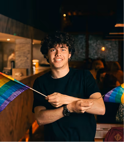 Team member holding rainbow Pride flags in a bar during Pride celebrations
