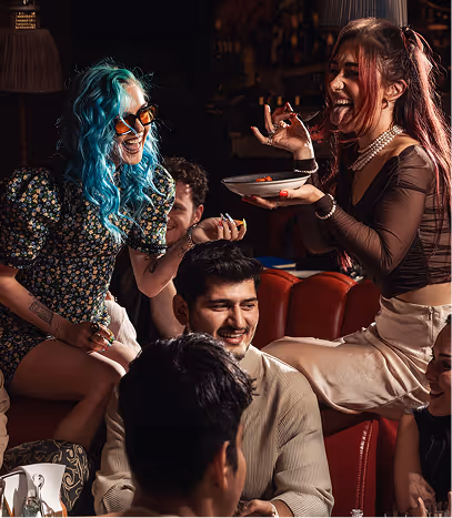 Friends laughing and sharing food at a table in a dimly lit bar