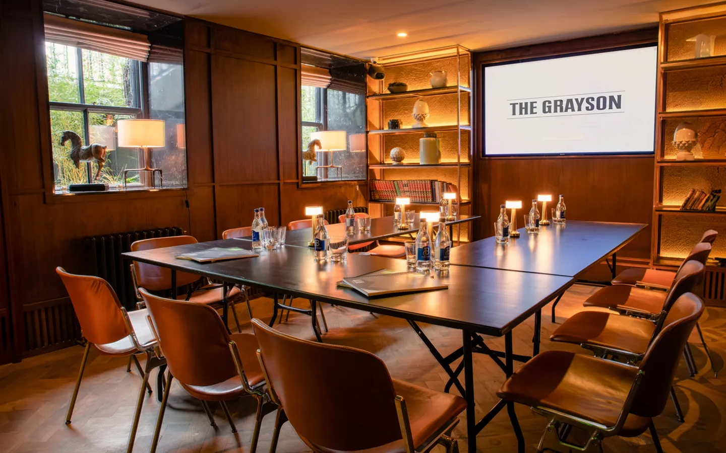 Private meeting room set boardroom-style with a presentation screen at The Grayson