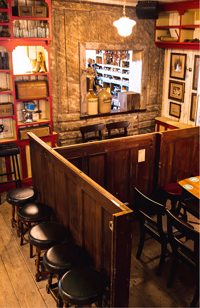 Wooden snug partition, leather-topped stools and hardware-shop shelving in a traditional pub