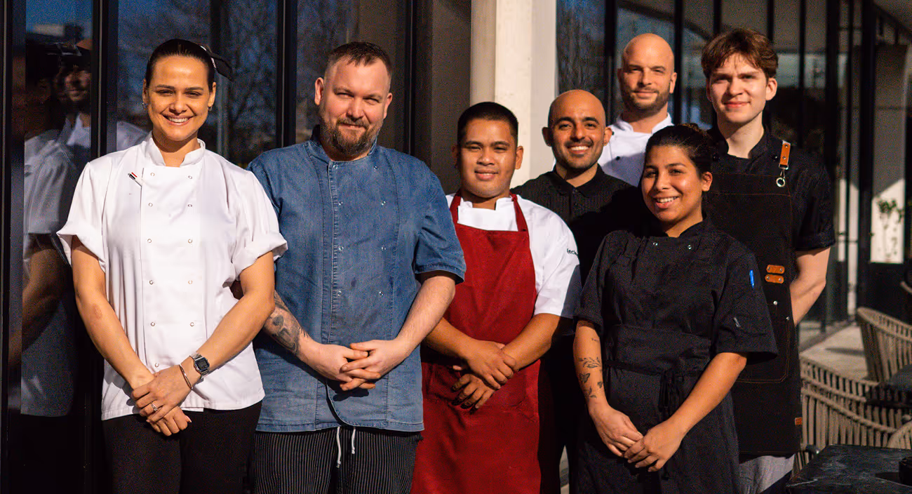 Chef team in whites and aprons standing outside a glass-fronted venue