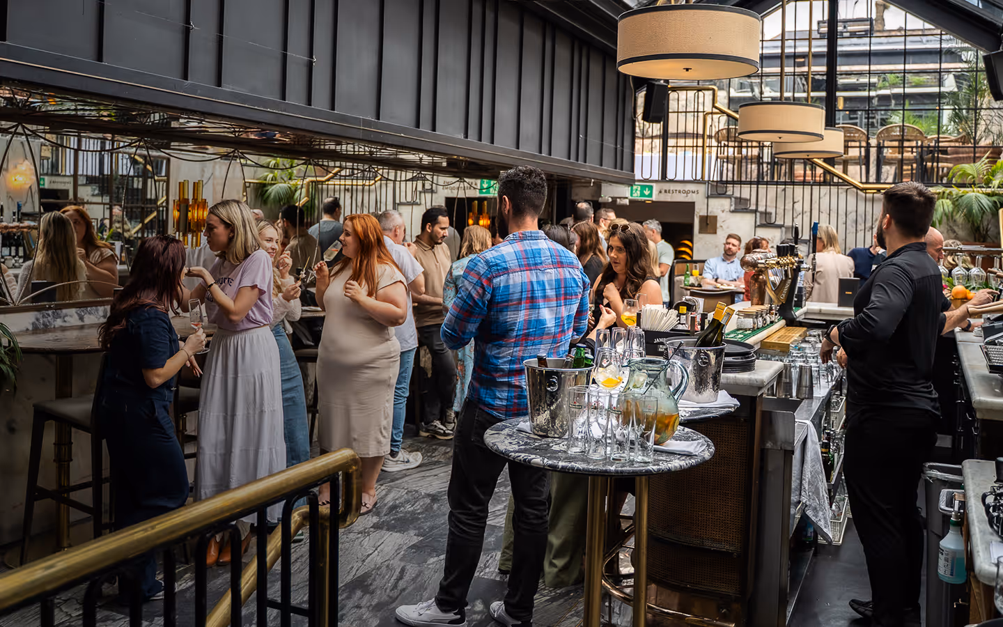 Guests drinking at the marble bar beneath the glazed atrium roof at The Grayson
