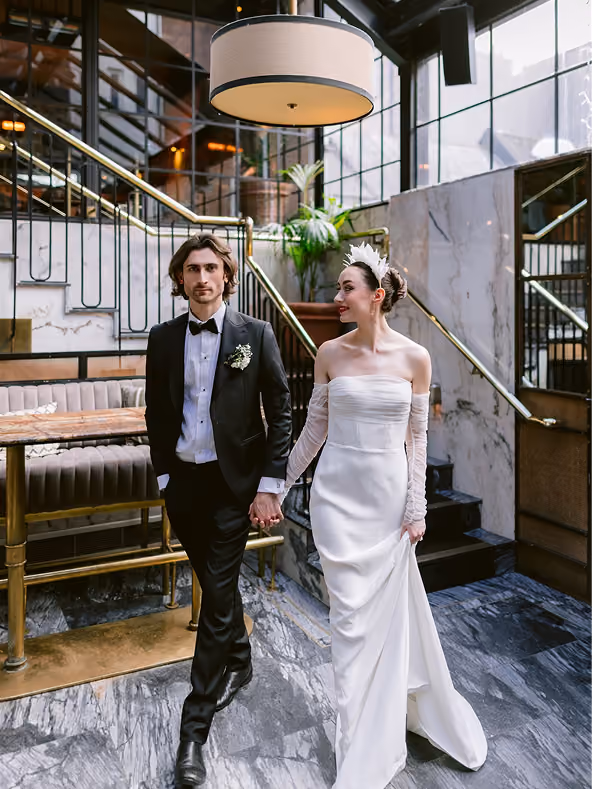 Bride and groom holding hands as they walk through a marble and brass staircase hall