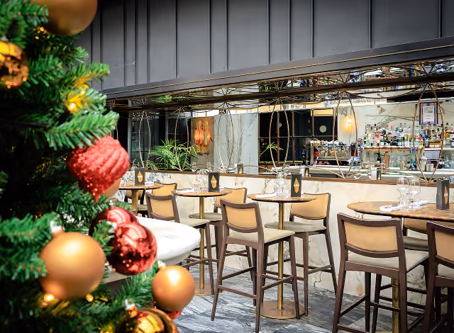 Christmas tree in red and gold beside high bar tables and stools at The Grayson