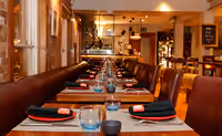 Long banquette table laid with red placemats in front of an open kitchen