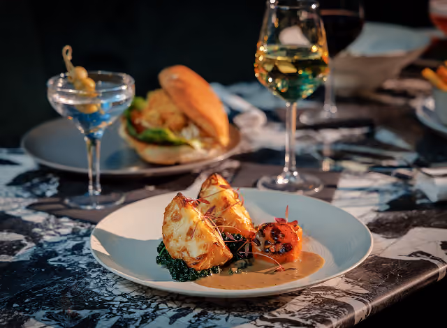 Plated white fish on greens beside a martini and a glass of white wine