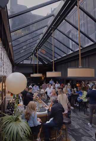 Guests mingling around a bar beneath a glazed pitched roof at a private event