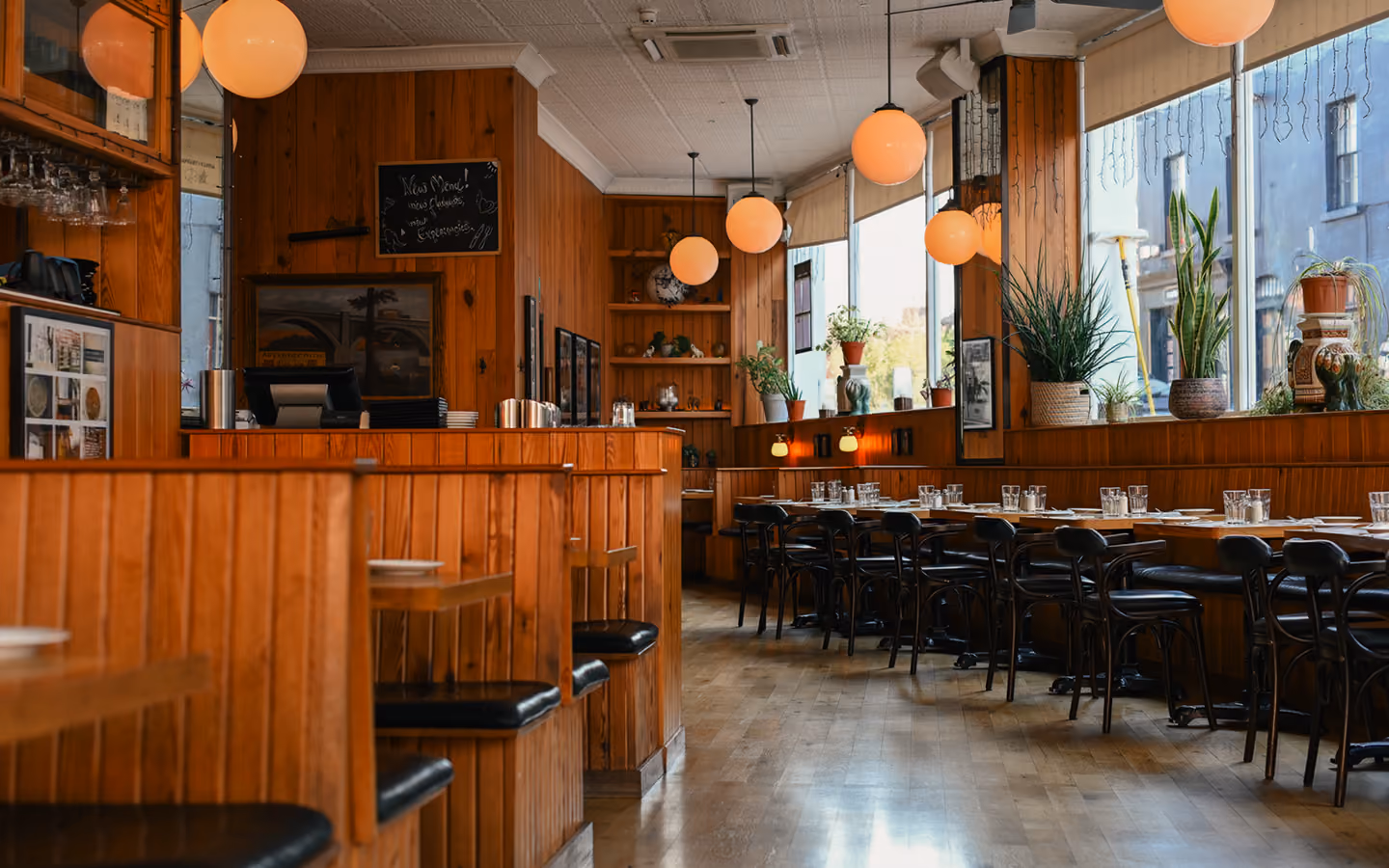Timber-panelled dining room with wooden booths, bentwood chairs and globe pendant lights