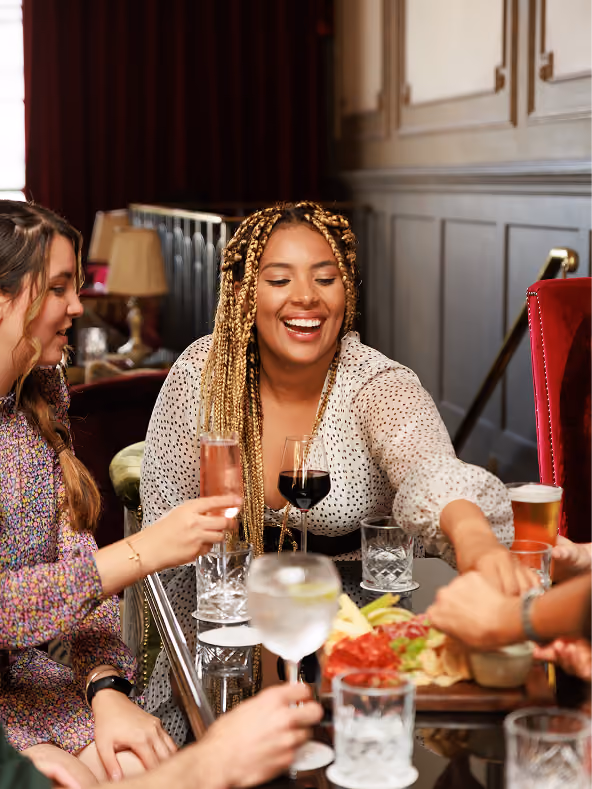 Friends laughing over cocktails and a sharing board in a wood-panelled dining room