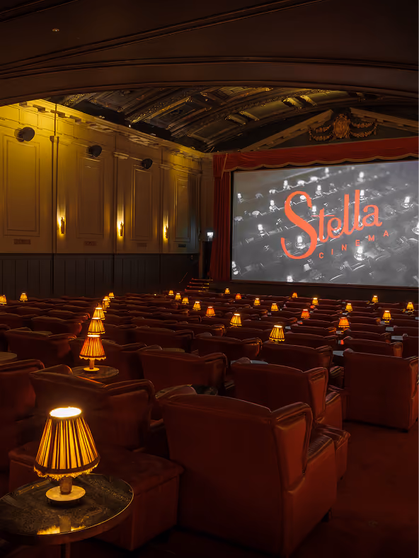 Rows of red leather armchairs and lamp-lit tables facing the screen at Stella Cinema