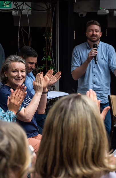 Guests applauding as a man gives a speech into a microphone at a wedding reception