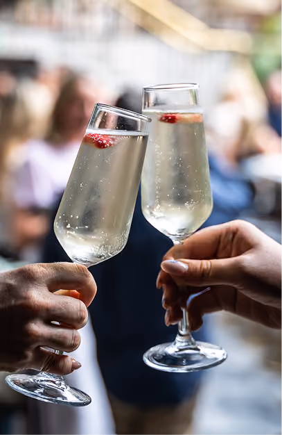 Two hands clinking sparkling wine flutes garnished with raspberries at a wedding reception