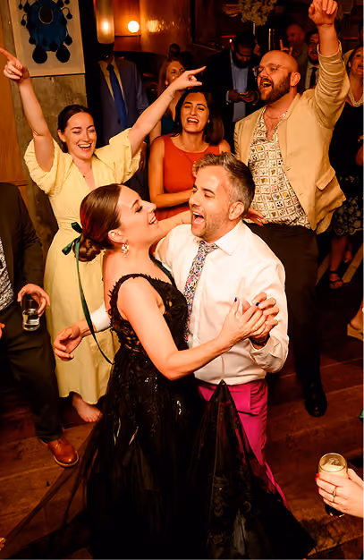 Guests dancing and cheering on the floor of a timber-clad room at a wedding party