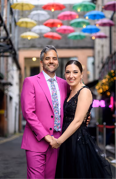 Couple in a magenta suit and black gown beneath a canopy of coloured umbrellas in a Dublin laneway