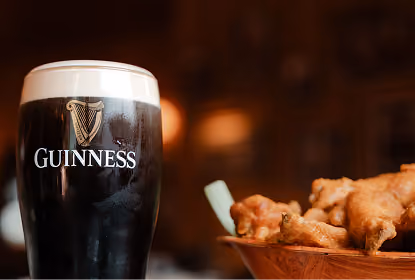 Pint of Guinness stout with a creamy head on the left and a bowl of fried chicken wings on the right in a dimly lit setting.