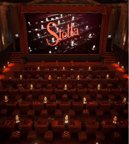 Interior view of an empty, dimly lit movie theatre with rows of plush red seats and small lamps on each seat, facing a large screen displaying the Stella Cinema logo.