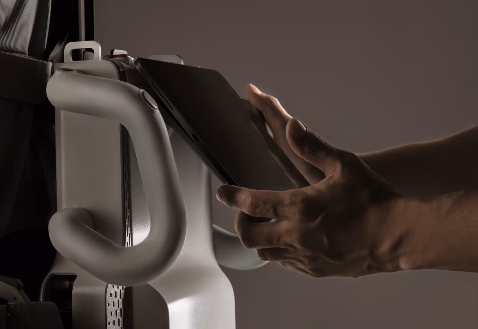 Hands placing a tablet device into a white docking station with curved handles.