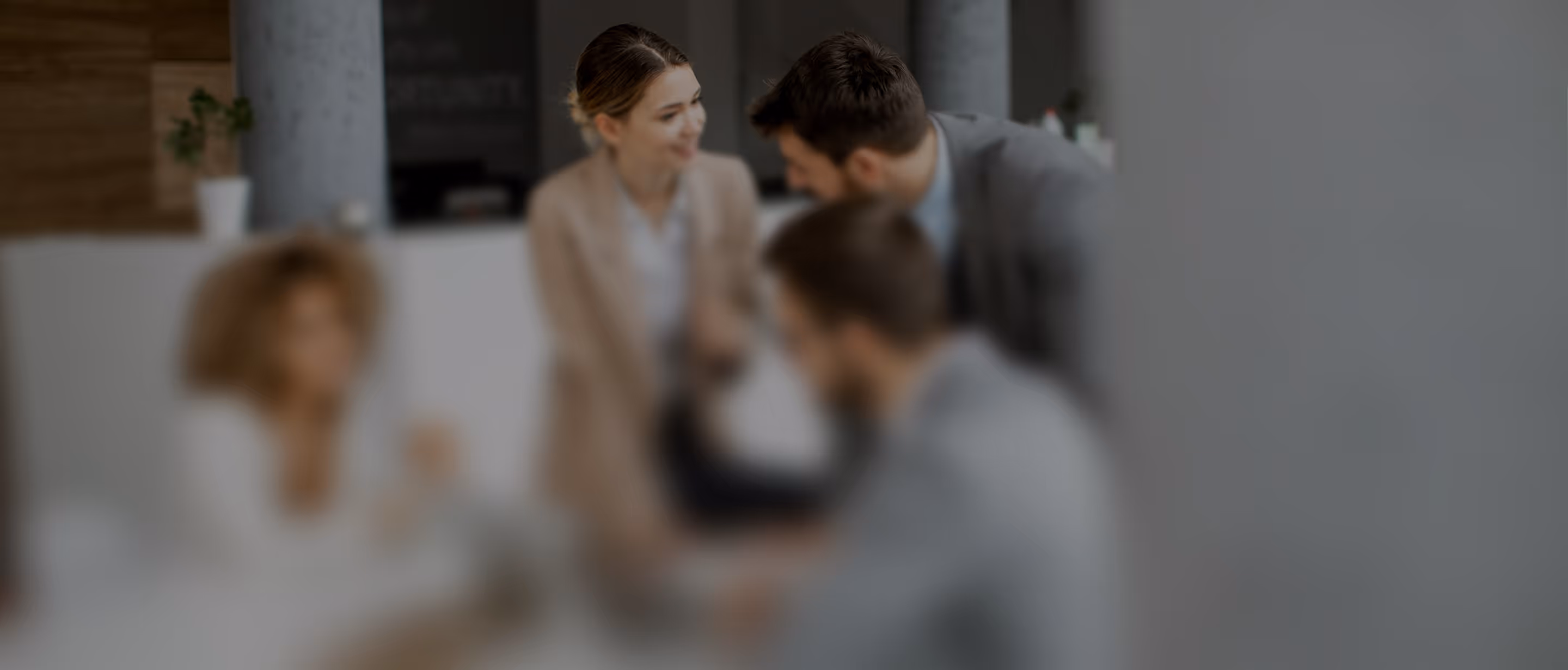Four business professionals in a modern office engaged in a discussion at a table.