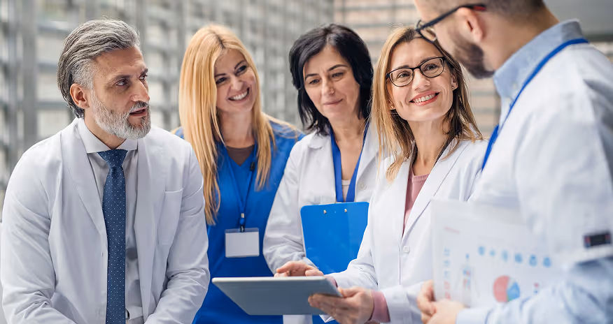 Group of diverse medical professionals discussing information on a tablet in a hospital corridor.