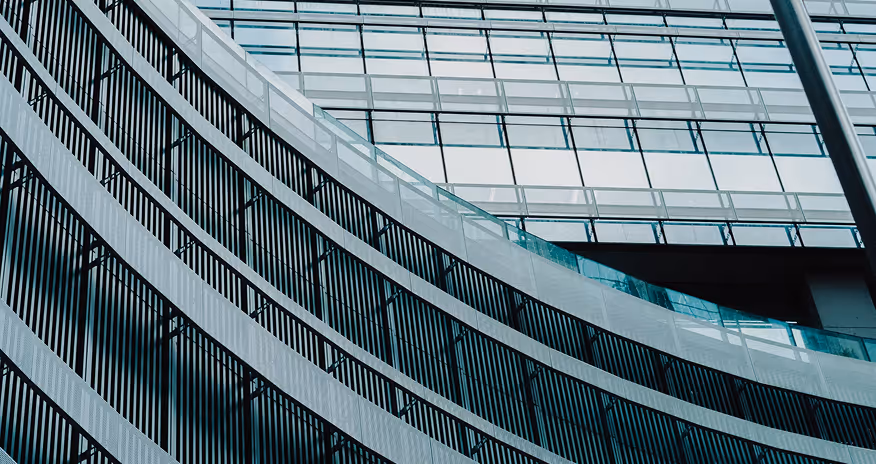 Curved modern building façade with glass panels and vertical black metal railings.