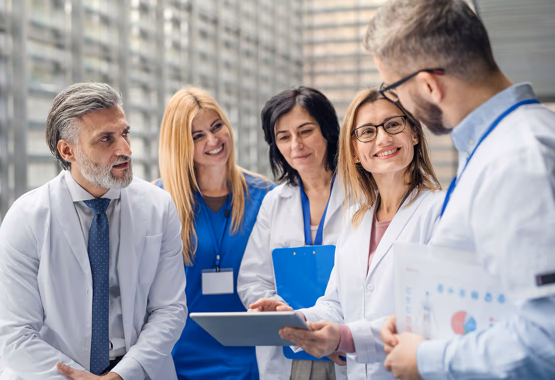 A diverse group of five medical professionals discussing data on a tablet and clipboard in a modern office.