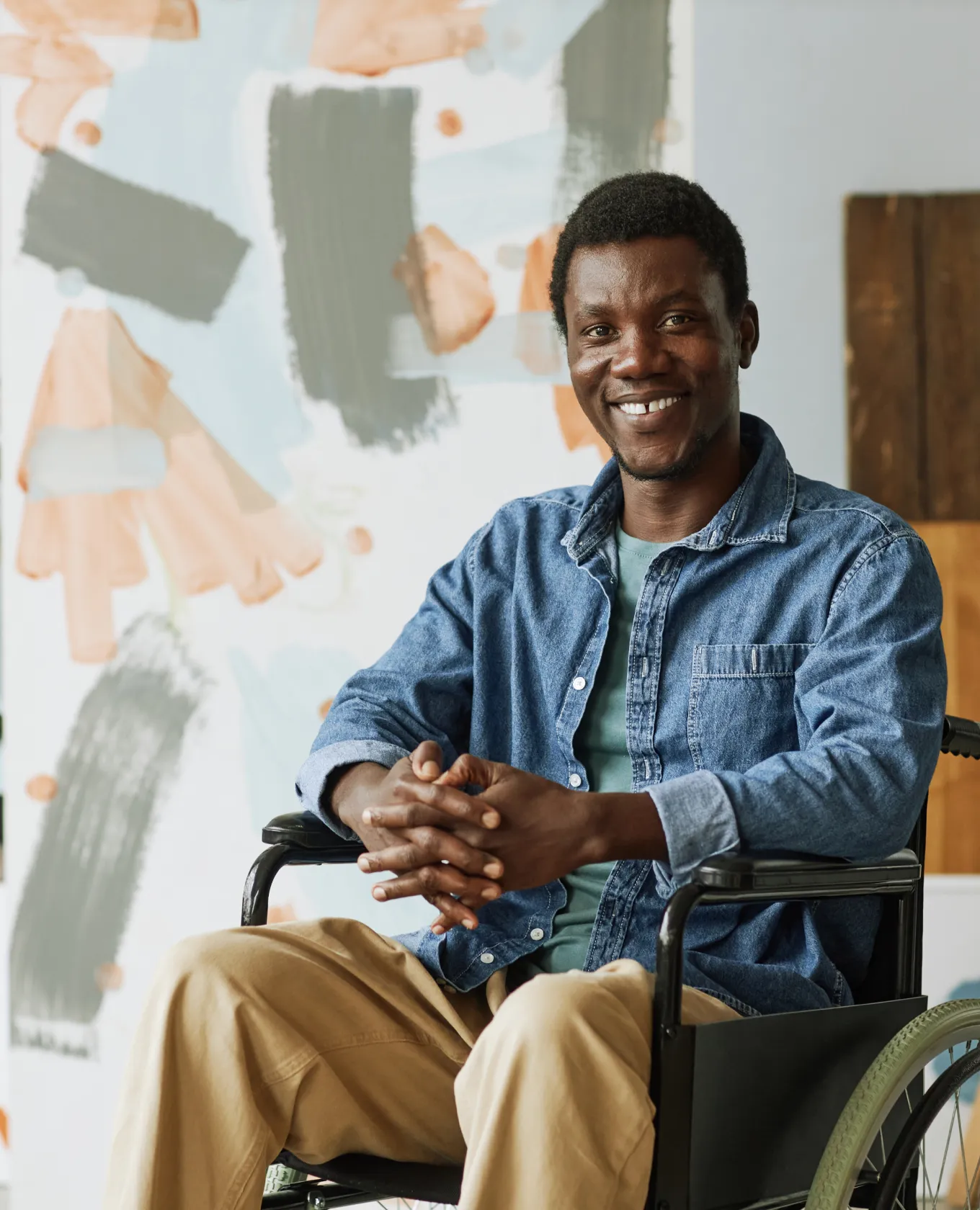 A smiling man in a wheelchair posing in front of his artwork.