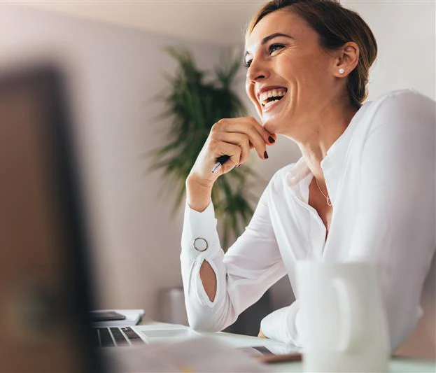 Donna sorridente mentre lavora al computer in un ambiente d'ufficio luminoso.