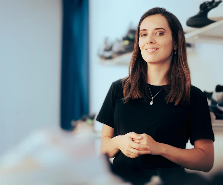 Donna sorridente con maglietta nera e collana in negozio di scarpe, con scaffali di scarpe sullo sfondo.