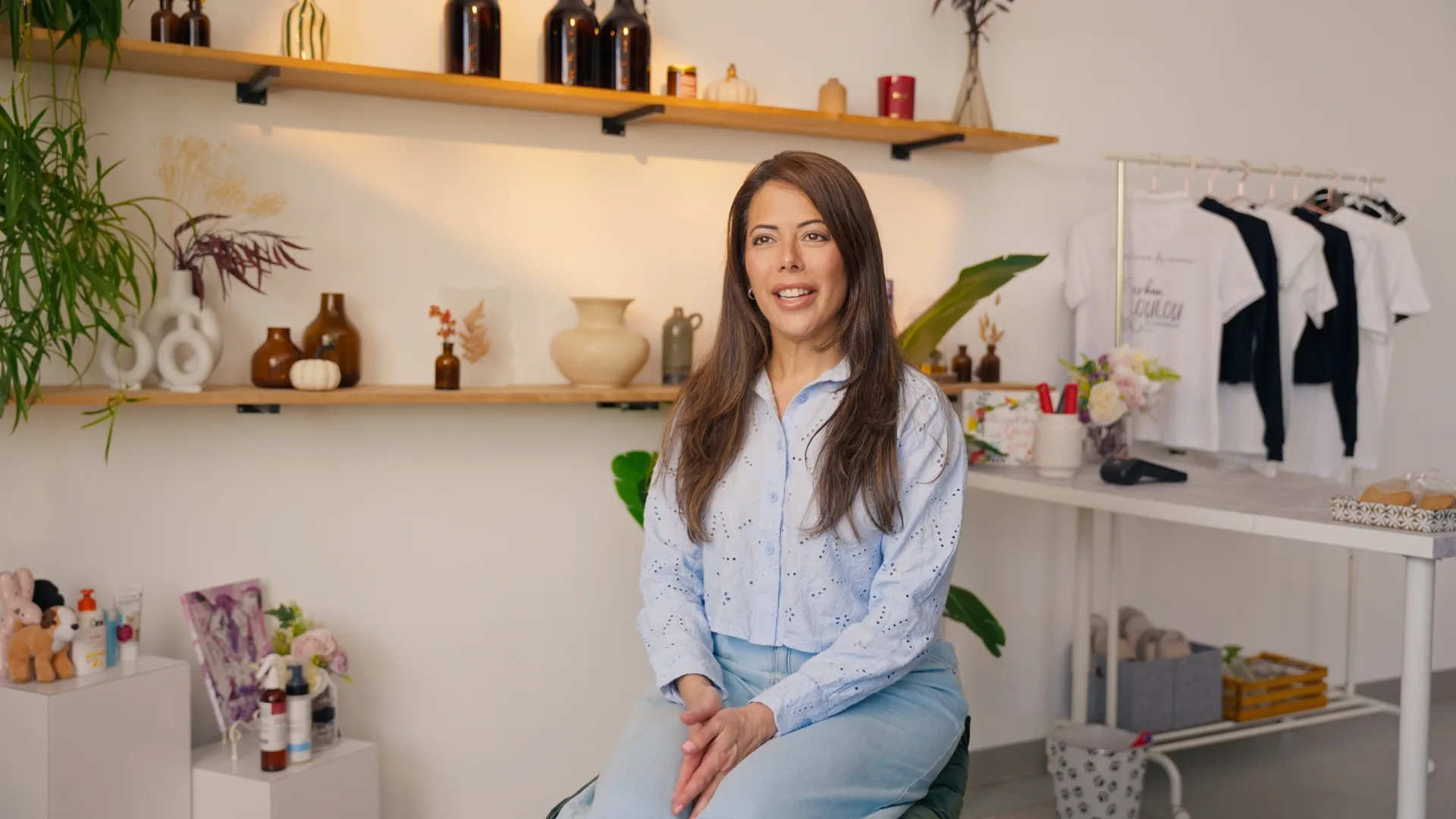 La commerçante assise au milieu de sa boutique, étagères de produits et portants derrière elle