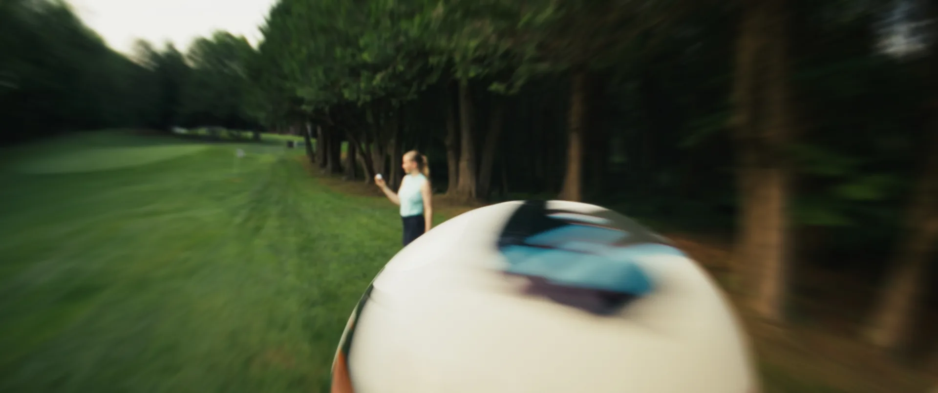 Balle de golf en gros plan filé, golfeuse en approche dans l'allée bordée d'arbres