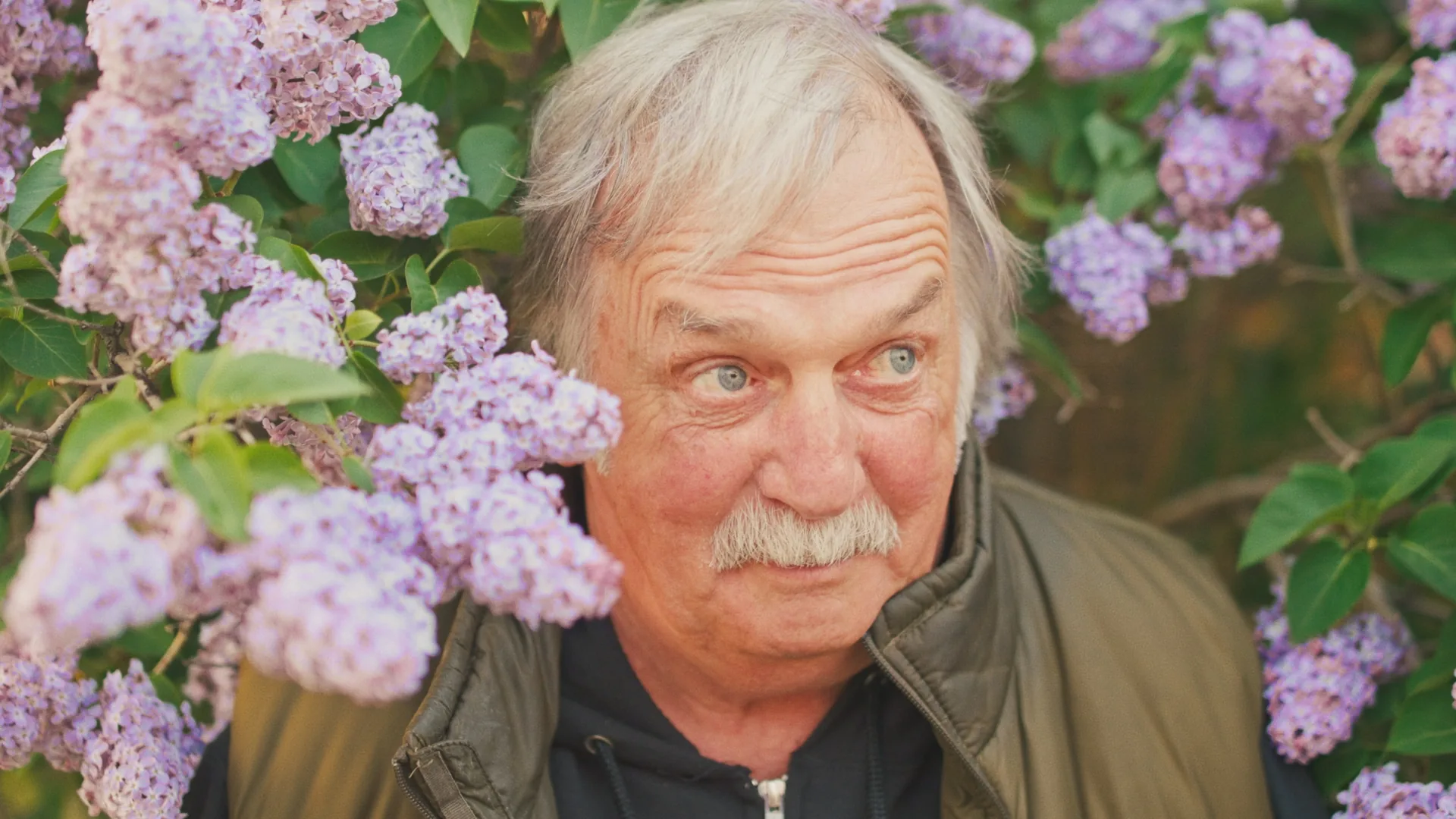 Portrait d'un homme âgé aux cheveux blancs entouré de lilas mauves en fleurs, court-métrage de Yann Reynolds
