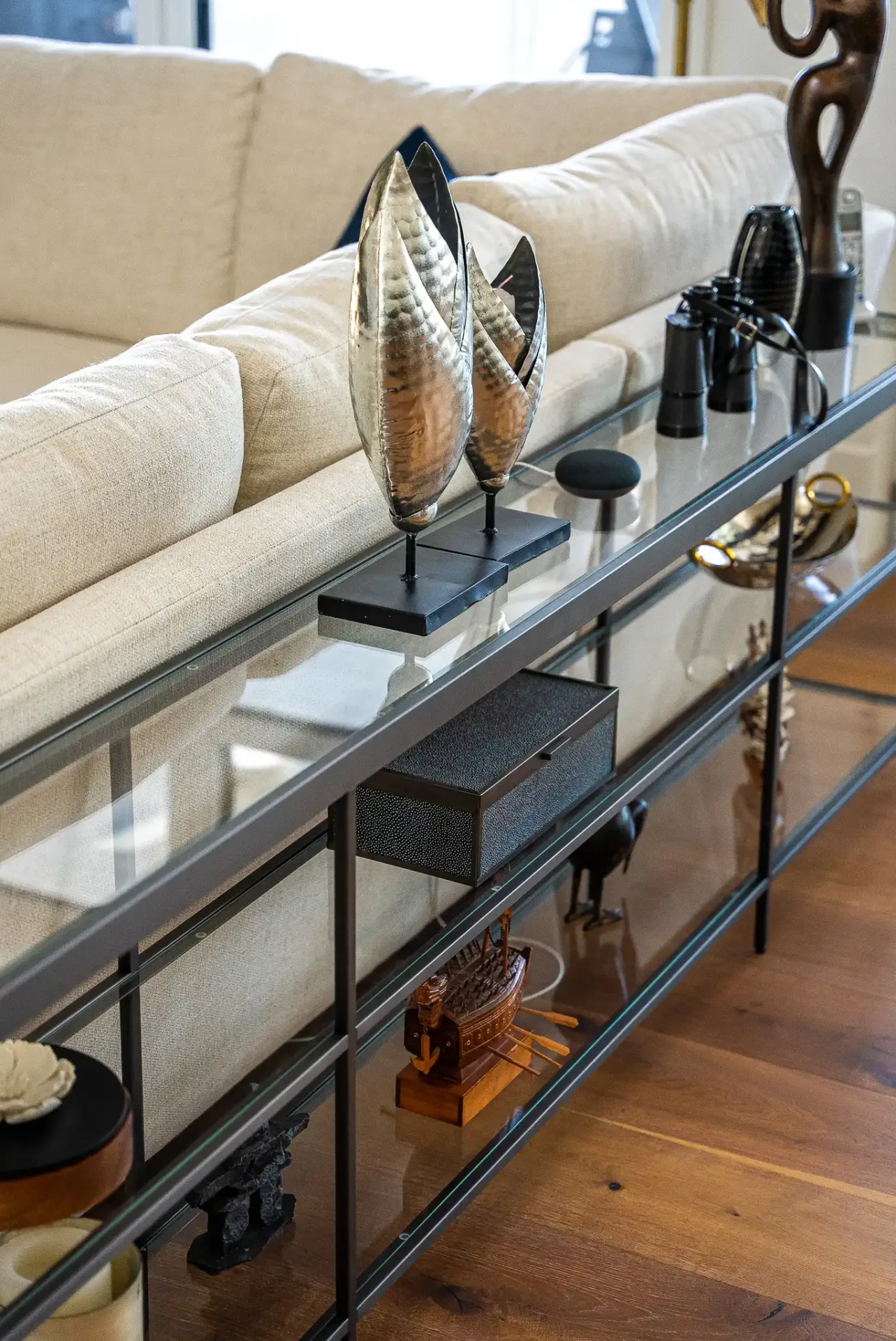 Console vitrée derrière un canapé crème, objets décoratifs alignés