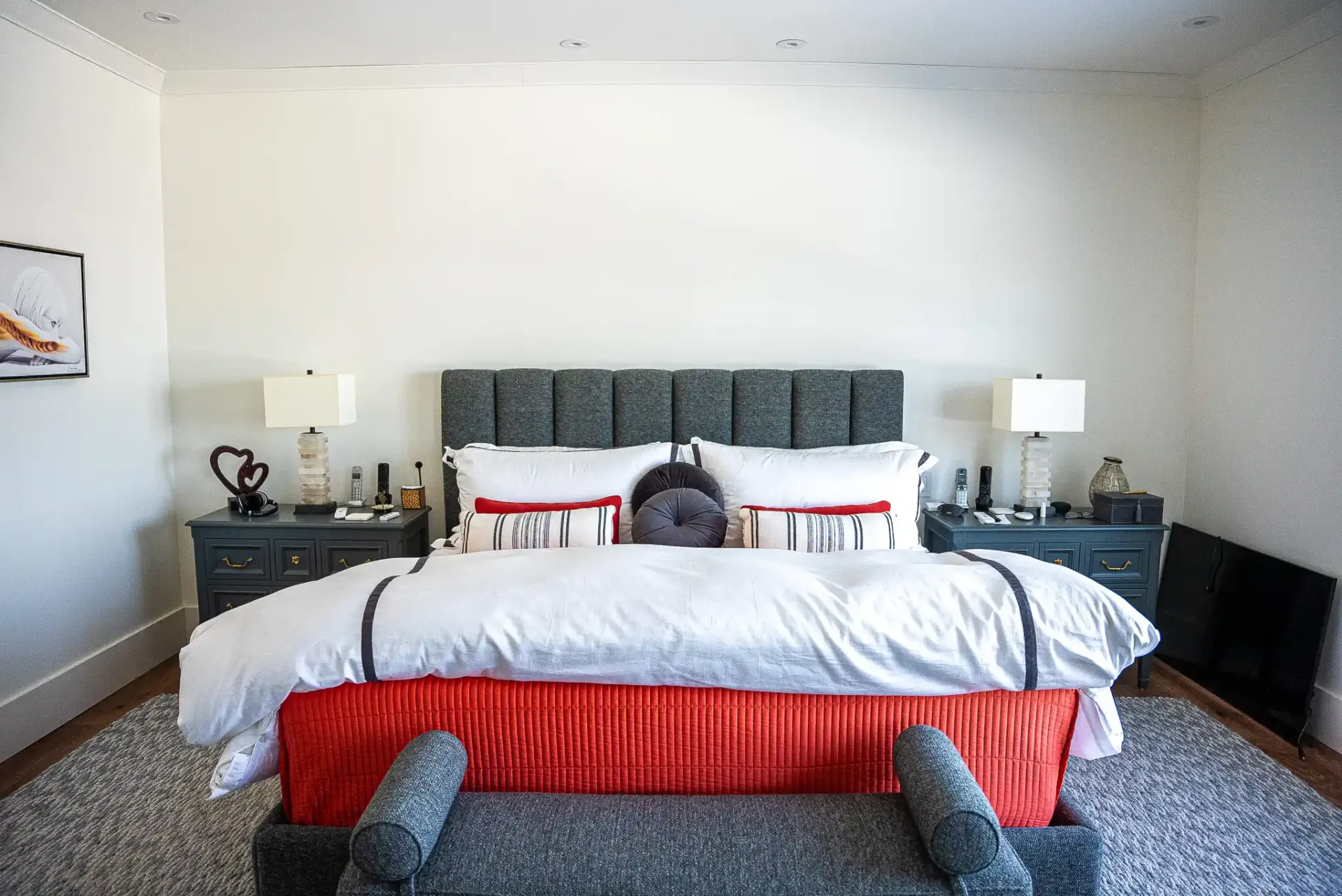 Chambre principale au lit capitonné gris et banc rouge au pied