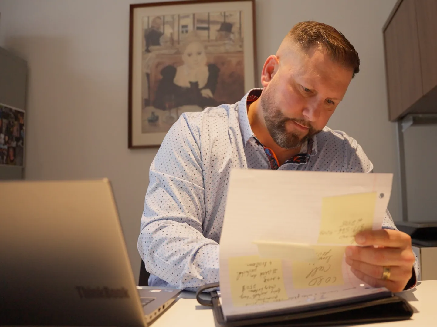 Courtier immobilier assis à son bureau, consultant un cartable couvert de notes autocollantes