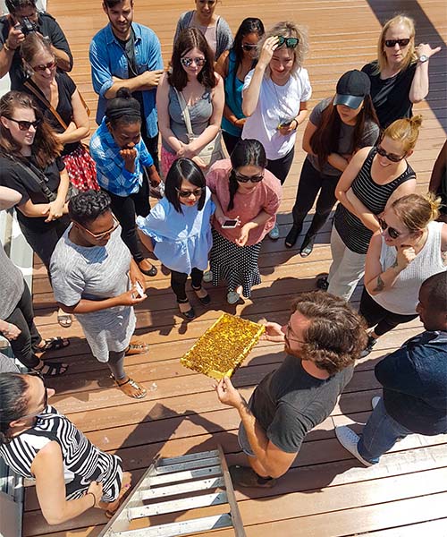 Un groupe de locataires sur un toit se presse autour de leur apiculteur pour voir leurs abeilles. entreprise d'apiculture urbaine