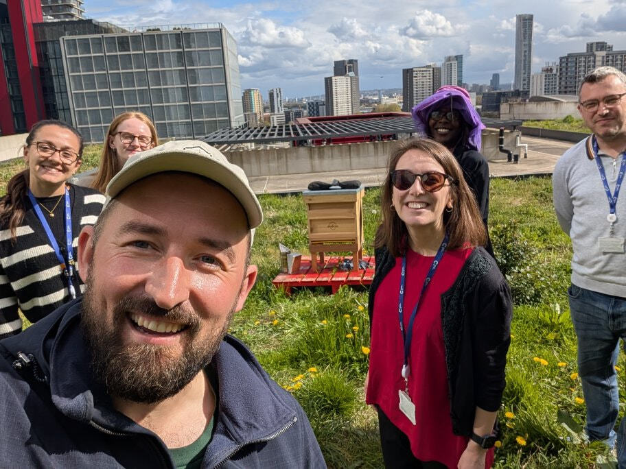Tenants and an Alvéole beekeeper gathered around the rooftop beehive at 2 Redman Place, with the London skyline behind them.