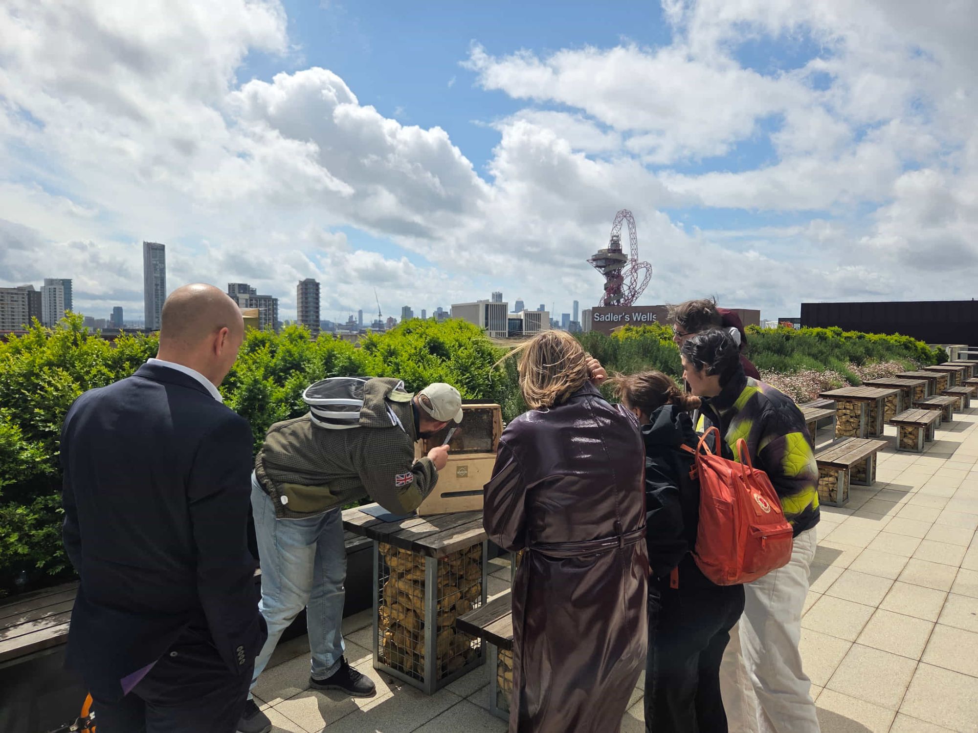 A beekeeper leads a rooftop hive session for office tenants on a green roof overlooking the London skyline.
