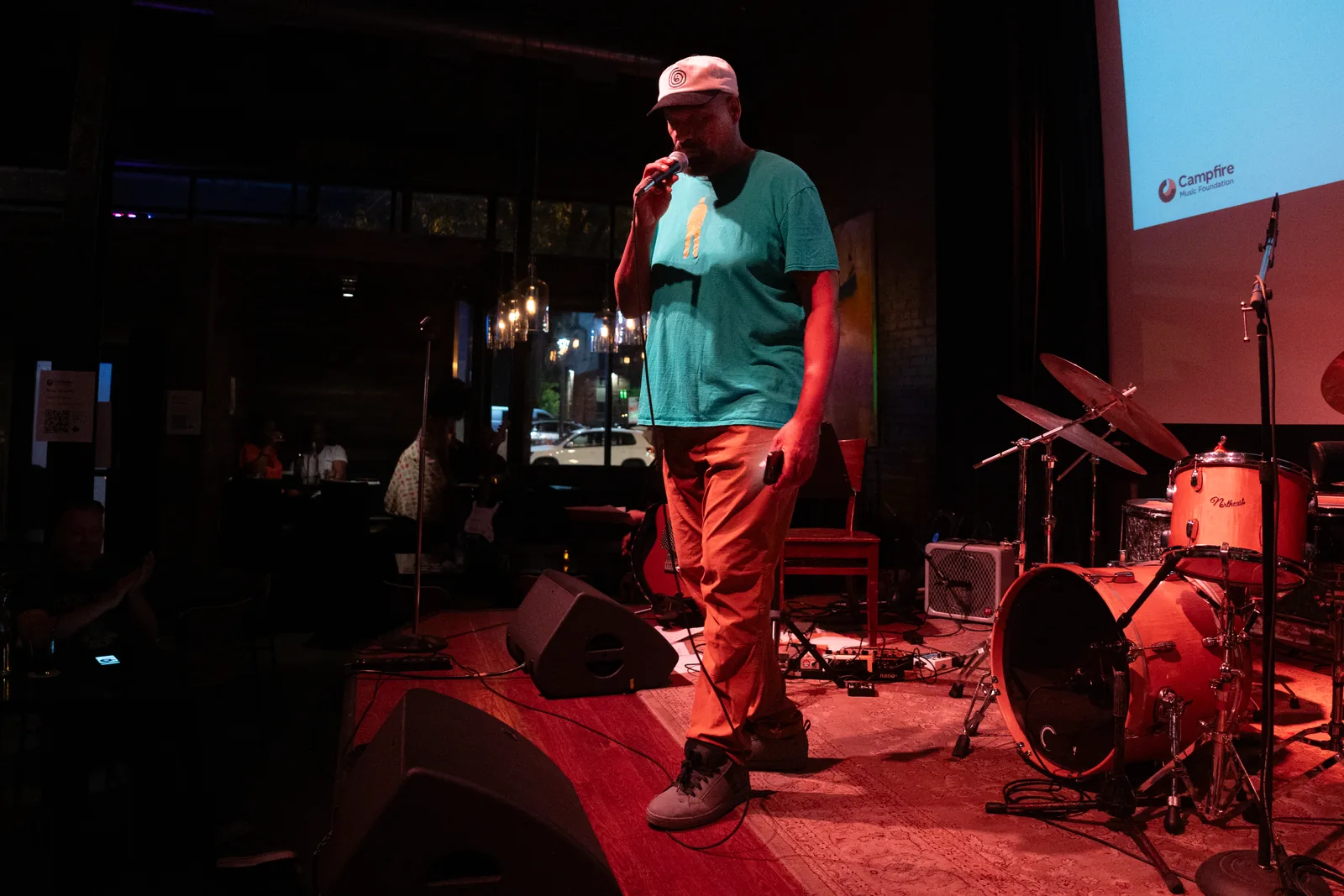 A performer on stage at a Campfire Music Foundation show, with the Campfire logo projected behind them.