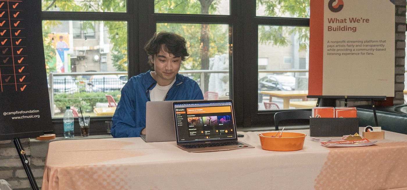 Davis Provost staffing the Campfire table at a community event, the pilot app open on a laptop.