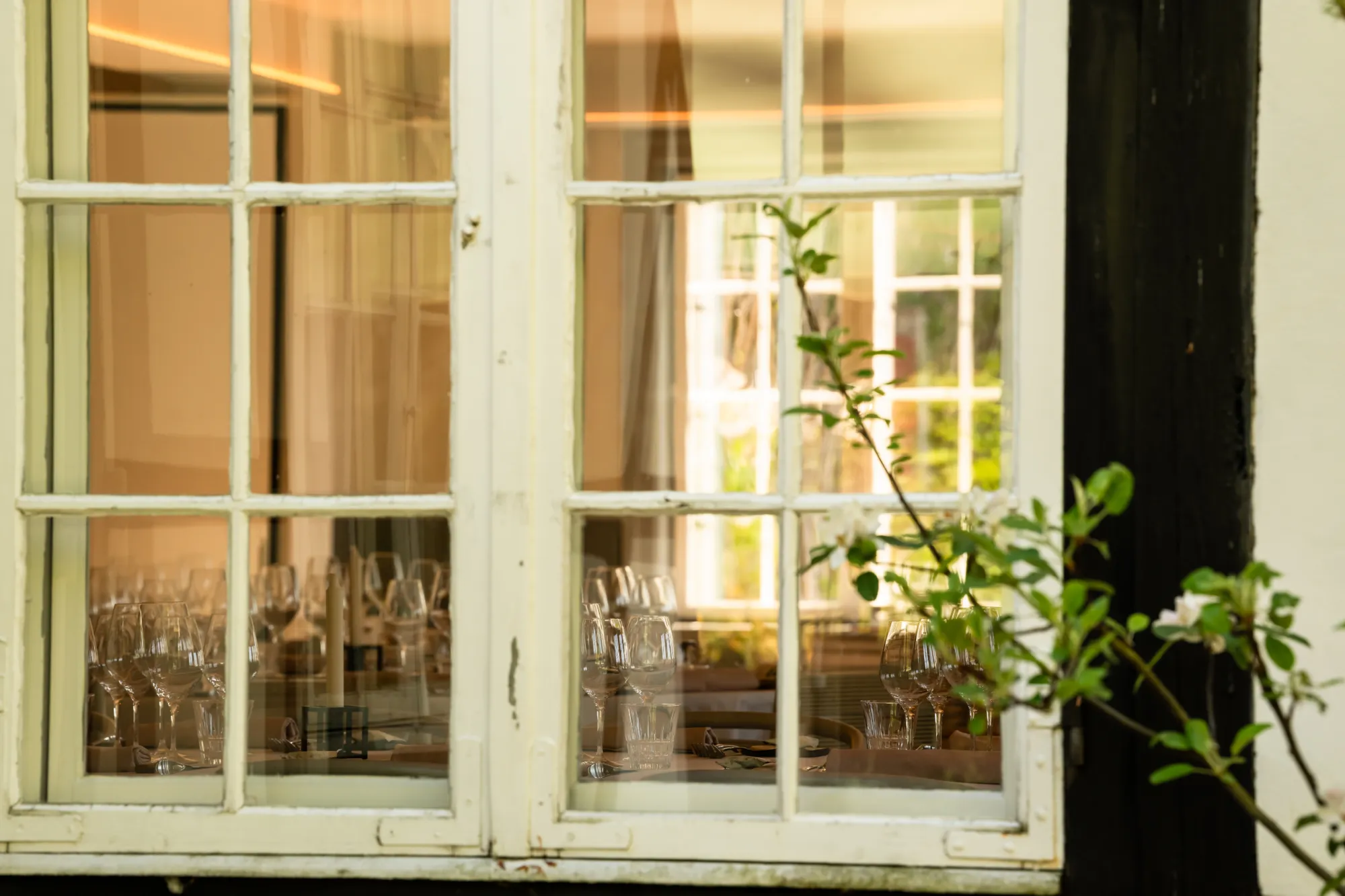Vindue med udsigt til et bord dækket med vinglas og stearinlys inde i en restaurant.