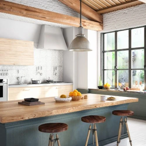 Bright modern kitchen with wooden island, three stools, hanging light, and large window with greenery outside.