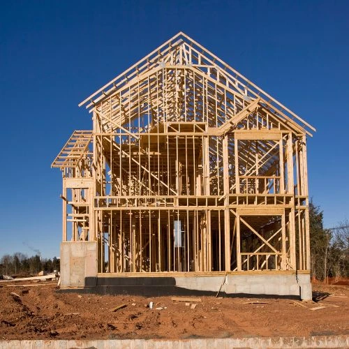 Wooden frame structure of a two-story house under construction on a clear day.