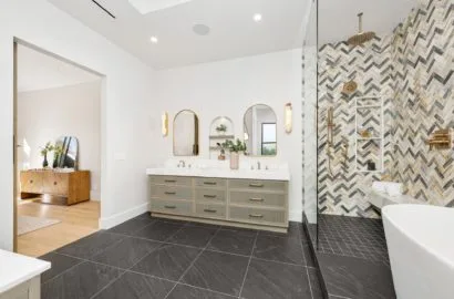 Modern bathroom with double vanity, arched mirrors, herringbone tiled shower, and freestanding tub.