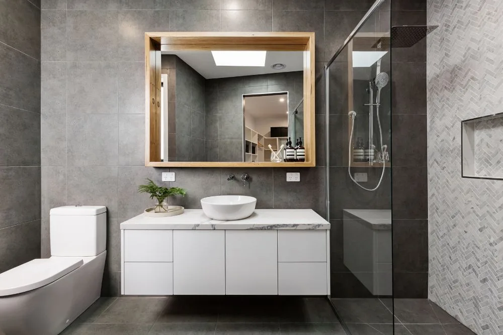 Modern bathroom with white toilet, floating vanity with vessel sink, large wooden framed mirror, and glass shower.