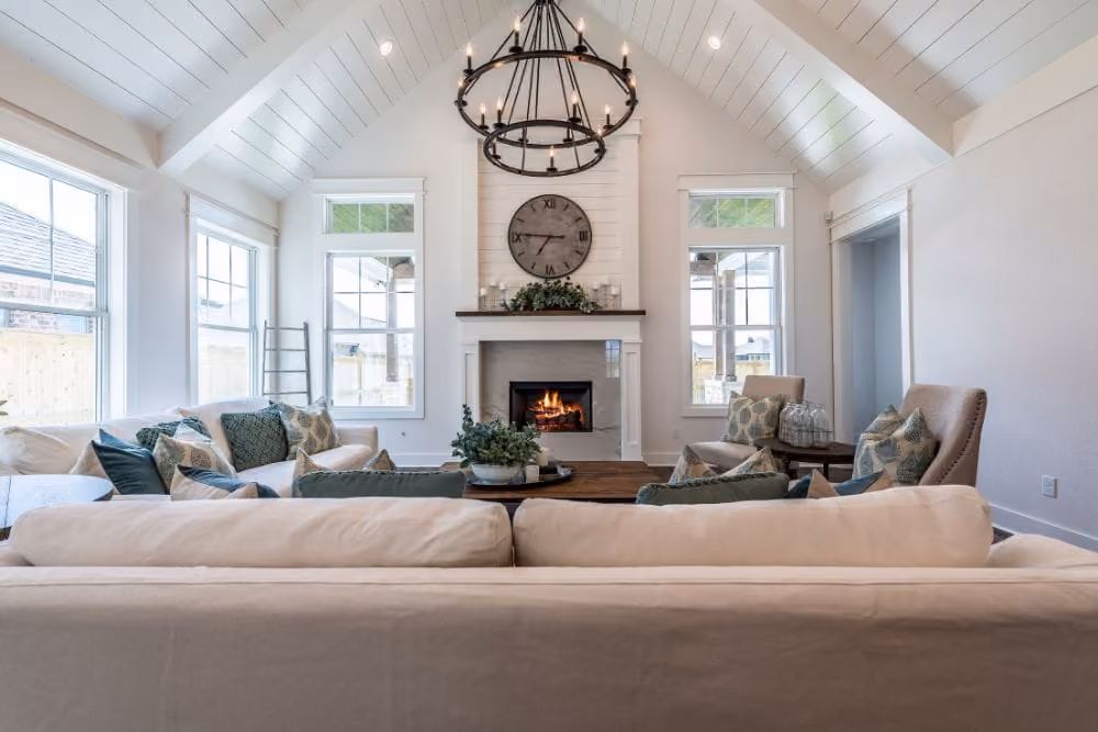 Bright living room with white vaulted ceilings, fireplace, beige sofas, and green patterned cushions.