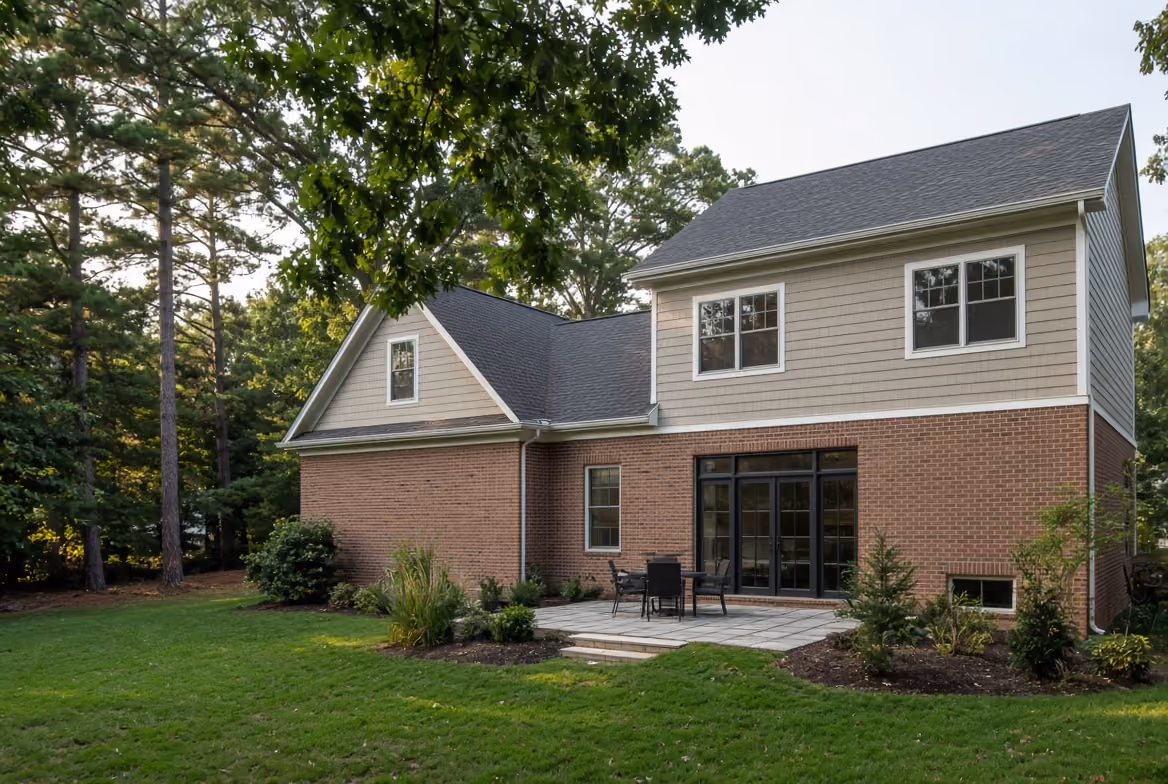 Backyard view of a brick and siding two-story house with a patio and patio furniture.