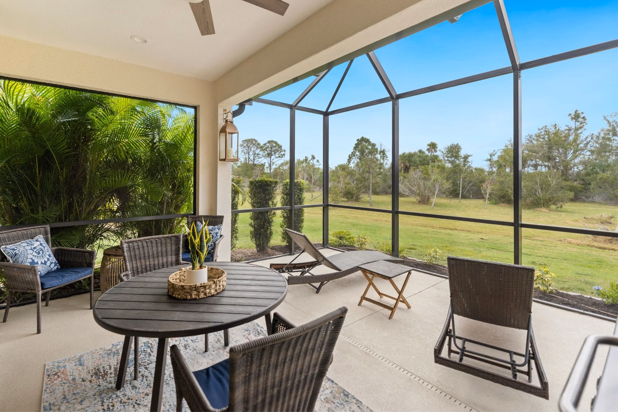 Screened patio with wicker chairs, a round table, lounge chairs, and a grassy backyard view.