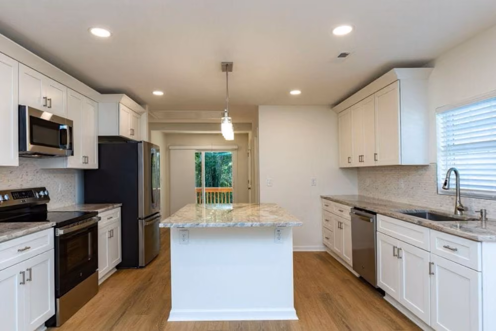 Bright kitchen with white cabinets, marble island, stainless appliances, and wood flooring.