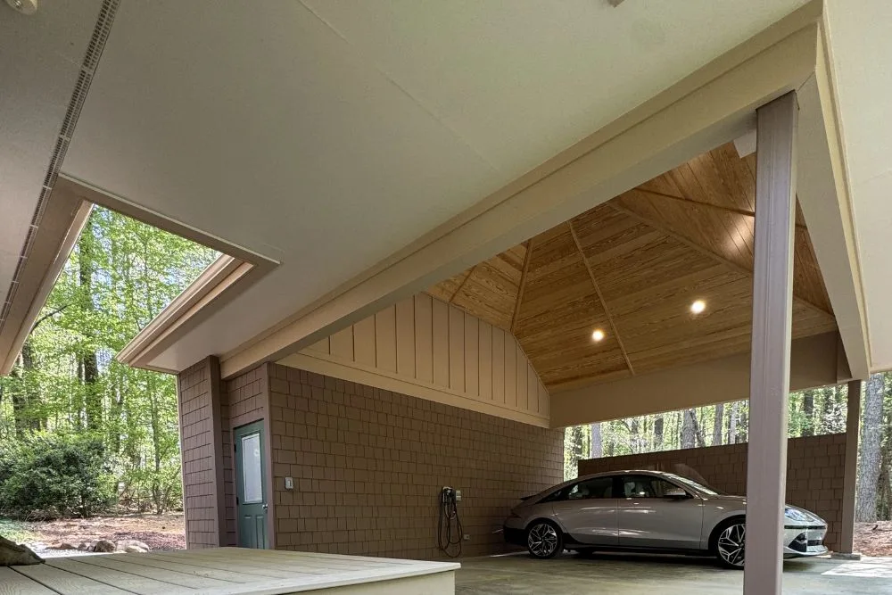 Modern carport with a wood-paneled vaulted ceiling and an electric vehicle parked inside near a green door.